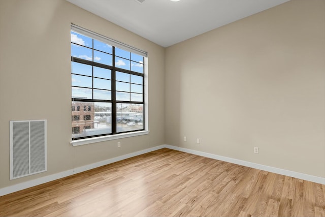 spare room featuring a healthy amount of sunlight, visible vents, baseboards, and wood finished floors