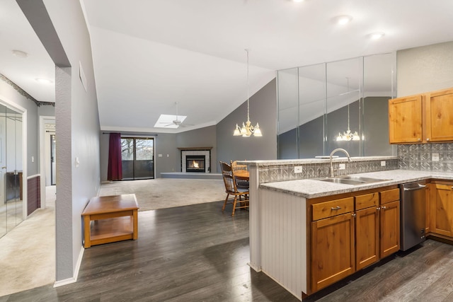 kitchen featuring dishwasher, a glass covered fireplace, open floor plan, a sink, and backsplash