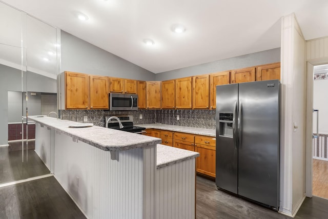 kitchen with lofted ceiling, a peninsula, light countertops, appliances with stainless steel finishes, and dark wood finished floors