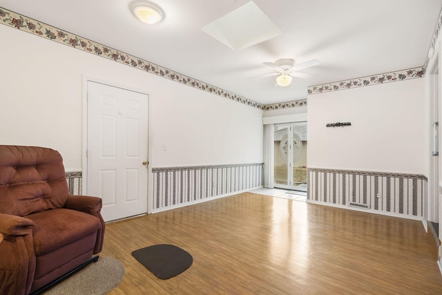 sitting room featuring a ceiling fan, a skylight, wainscoting, and wood finished floors