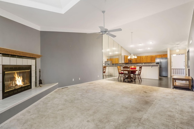 living area featuring ceiling fan with notable chandelier, vaulted ceiling, carpet flooring, and a tile fireplace