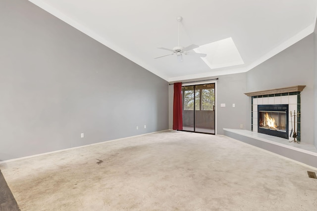 unfurnished living room featuring lofted ceiling with skylight, carpet flooring, a fireplace, and a ceiling fan