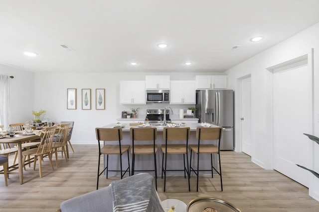 kitchen with a breakfast bar area, white cabinets, appliances with stainless steel finishes, light wood finished floors, and a center island with sink