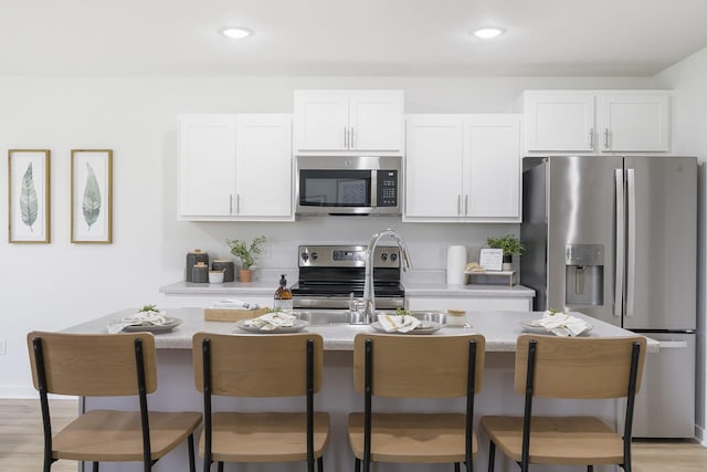 kitchen with appliances with stainless steel finishes, a breakfast bar, white cabinetry, and a center island with sink