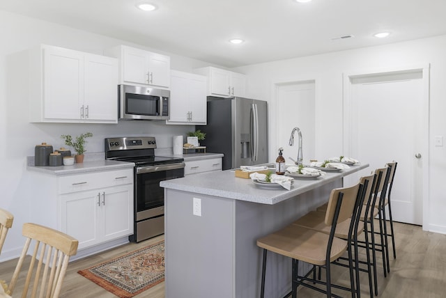 kitchen with light wood-style flooring, stainless steel appliances, a breakfast bar, white cabinetry, and light countertops