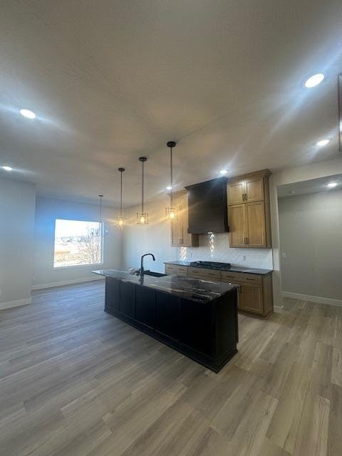 kitchen featuring light wood finished floors, baseboards, backsplash, and exhaust hood