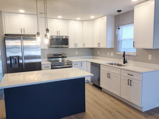 kitchen with pendant lighting, light wood-style flooring, appliances with stainless steel finishes, white cabinetry, and a sink