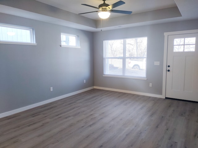 foyer entrance with ceiling fan, a tray ceiling, wood finished floors, and baseboards