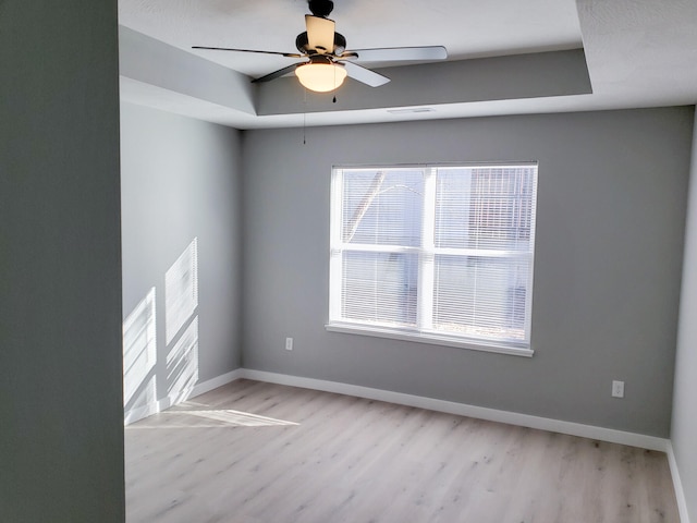 empty room featuring light wood-style floors, ceiling fan, baseboards, and a raised ceiling