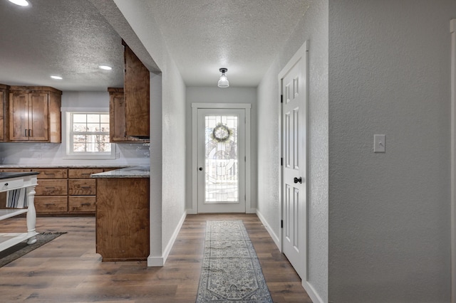 doorway to outside with dark wood finished floors, a textured wall, a textured ceiling, and baseboards