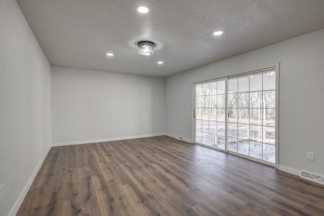 spare room featuring dark wood-style floors, visible vents, a textured ceiling, and baseboards