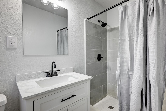 full bath with a textured wall, a tile shower, and vanity