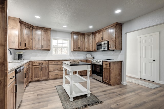 kitchen with a textured ceiling, recessed lighting, stainless steel appliances, a sink, and light wood-type flooring