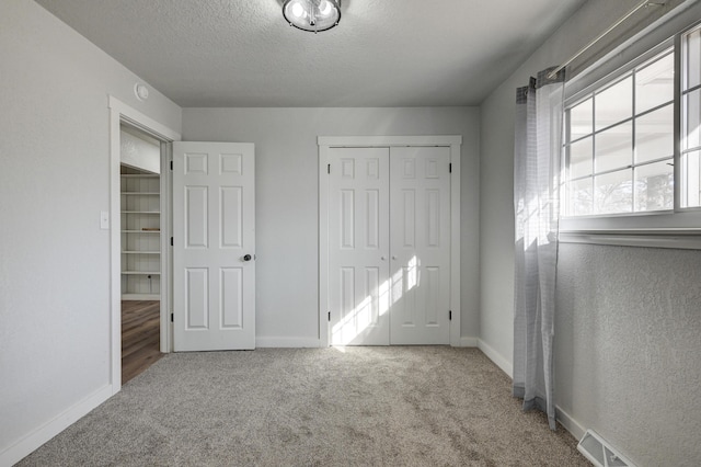 unfurnished bedroom featuring carpet floors, a closet, a textured ceiling, and baseboards