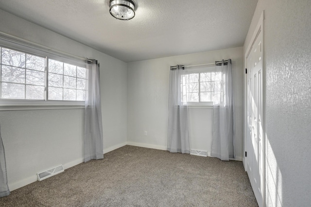 empty room with carpet floors, baseboards, visible vents, and a textured ceiling