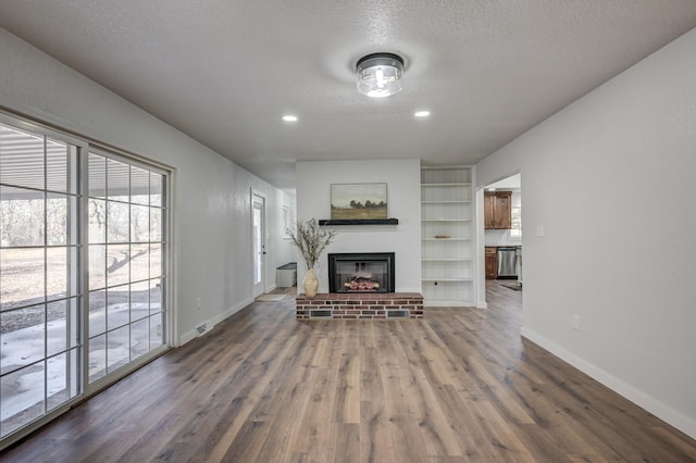 unfurnished living room featuring built in features, baseboards, a glass covered fireplace, wood finished floors, and a textured ceiling