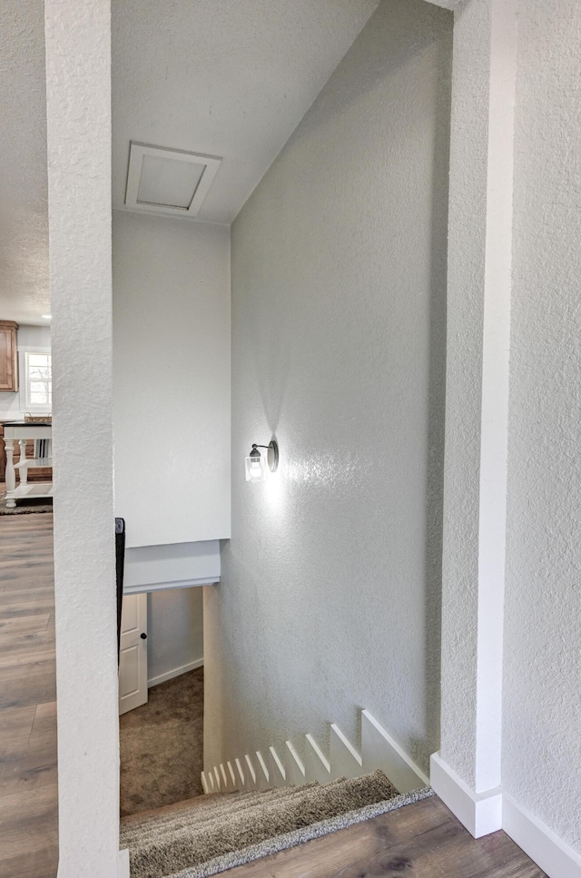 stairway featuring attic access, a textured wall, and baseboards