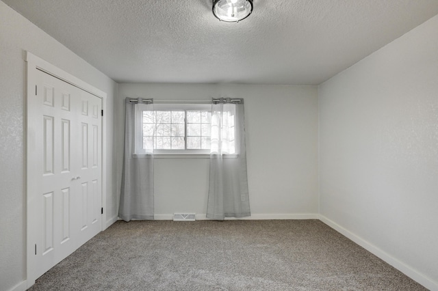 carpeted spare room with visible vents, a textured ceiling, and baseboards