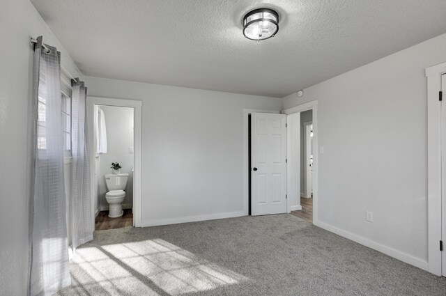 unfurnished bedroom featuring ensuite bath, a textured ceiling, baseboards, and carpet flooring