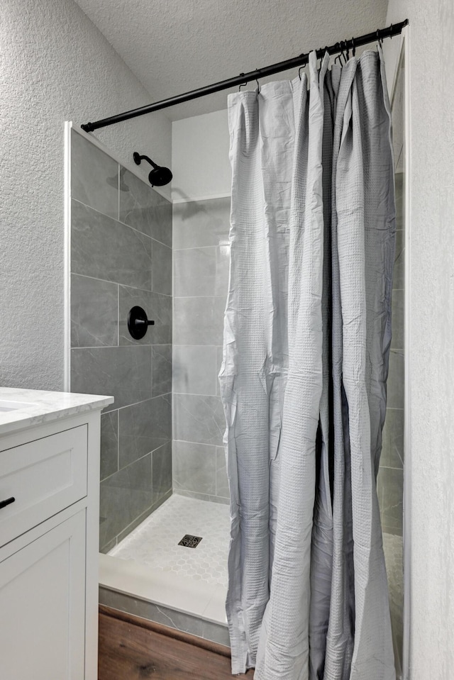 full bathroom featuring vanity, a tile shower, a textured ceiling, and a textured wall