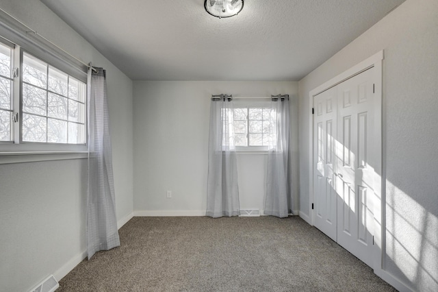 unfurnished bedroom featuring carpet, visible vents, a textured ceiling, and baseboards