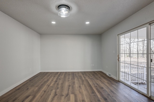 spare room featuring dark wood-type flooring, visible vents, a textured ceiling, and baseboards