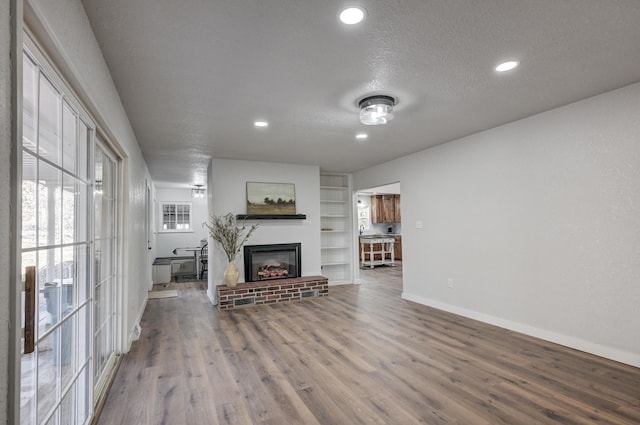 living area featuring built in features, a fireplace with raised hearth, a textured ceiling, wood finished floors, and baseboards