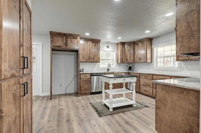 kitchen with stainless steel dishwasher, brown cabinetry, a sink, and light wood-style floors