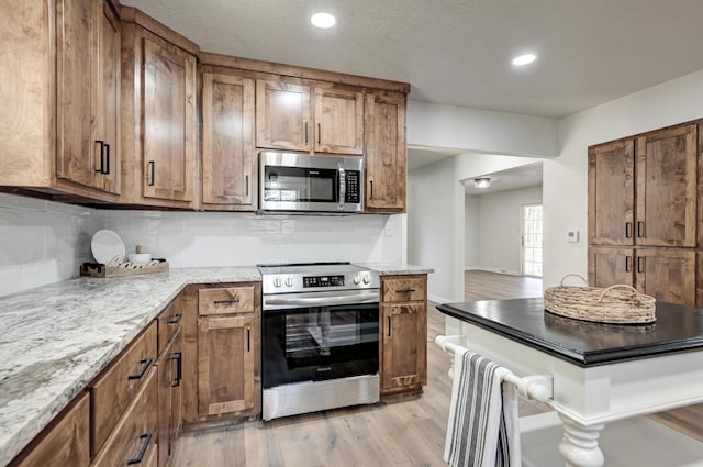 kitchen with recessed lighting, backsplash, appliances with stainless steel finishes, brown cabinetry, and light wood-type flooring