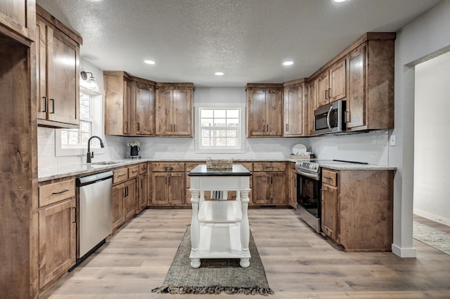 kitchen with stainless steel appliances, a healthy amount of sunlight, a sink, and light wood finished floors