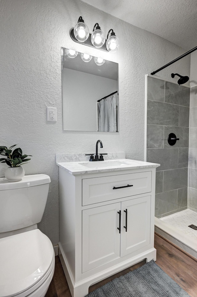 bathroom with a textured wall, tiled shower, vanity, and toilet