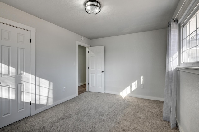 unfurnished bedroom with carpet flooring, a textured ceiling, and baseboards