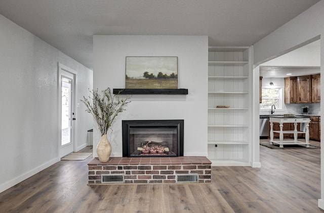 living room with visible vents, baseboards, wood finished floors, a brick fireplace, and built in shelves