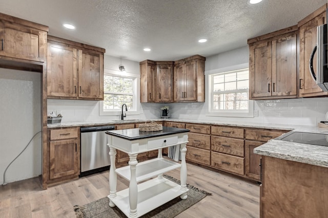 kitchen with stainless steel appliances, light wood finished floors, brown cabinetry, and a sink