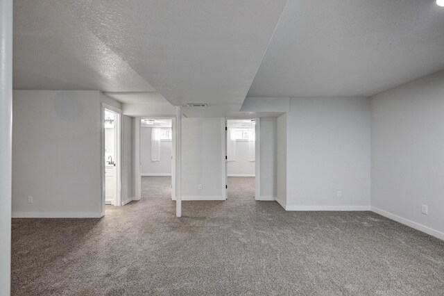 basement with carpet, a textured ceiling, visible vents, and baseboards