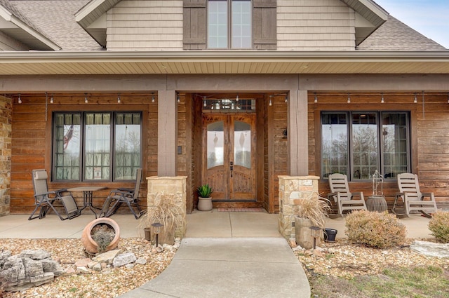 doorway to property with covered porch, french doors, and roof with shingles