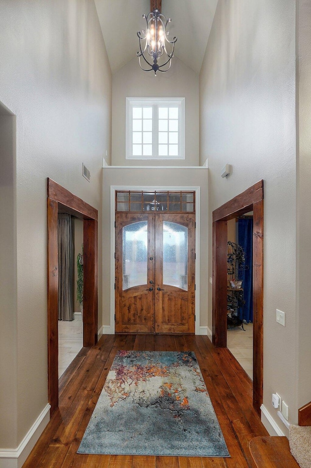 foyer featuring an inviting chandelier, wood-type flooring, visible vents, and high vaulted ceiling