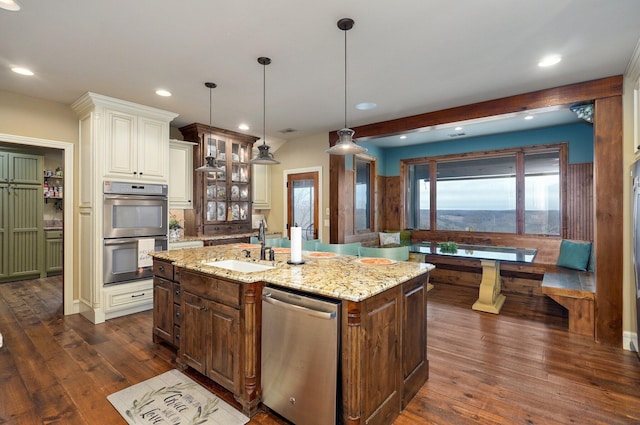 kitchen featuring a center island with sink, glass insert cabinets, dark wood-style flooring, stainless steel appliances, and a sink