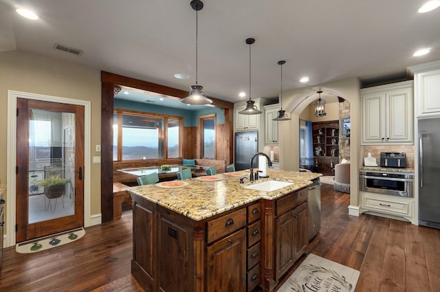 kitchen featuring arched walkways, dark wood finished floors, stainless steel appliances, visible vents, and a sink