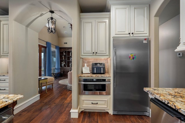 kitchen with a notable chandelier, dark wood finished floors, backsplash, appliances with stainless steel finishes, and light stone countertops