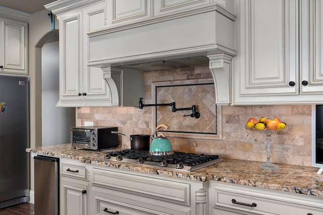 kitchen with light stone counters, a toaster, tasteful backsplash, appliances with stainless steel finishes, and premium range hood