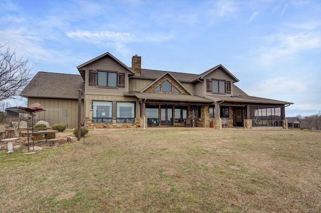 rear view of house with a yard, a chimney, a patio, board and batten siding, and a sunroom