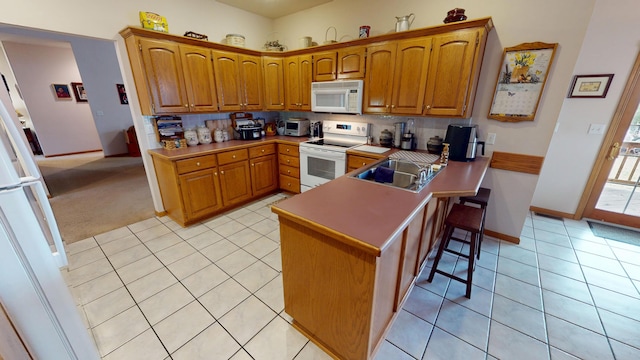 kitchen with a peninsula, white appliances, brown cabinetry, and a kitchen breakfast bar