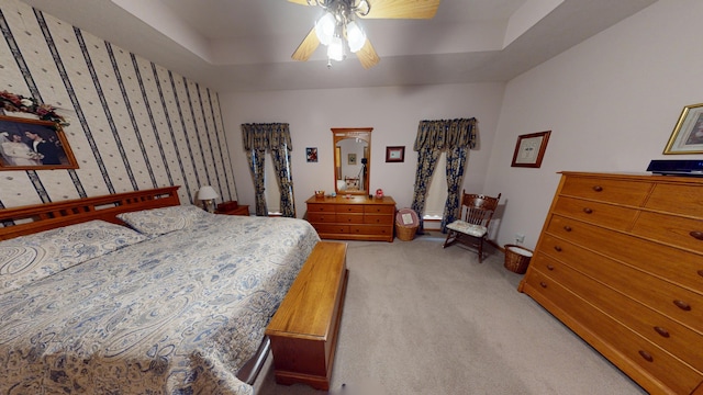 bedroom featuring ceiling fan, light carpet, baseboards, a tray ceiling, and wallpapered walls