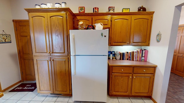 kitchen featuring light tile patterned floors, baseboards, brown cabinetry, and freestanding refrigerator