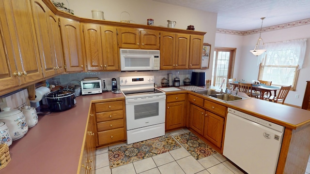 kitchen featuring a peninsula, white appliances, brown cabinets, and a sink