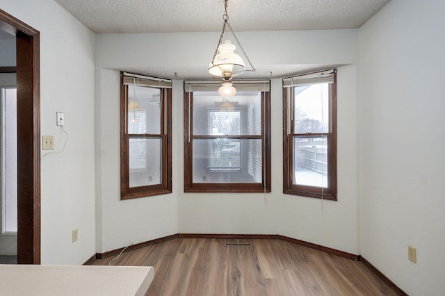 unfurnished dining area with visible vents, a textured ceiling, baseboards, and wood finished floors