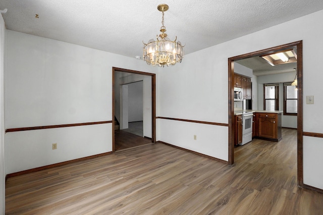 spare room with light wood-style floors, baseboards, a textured ceiling, and an inviting chandelier