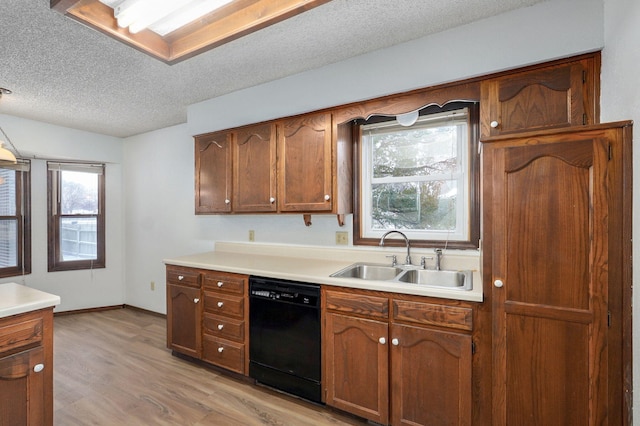 kitchen with black dishwasher, light countertops, light wood-style flooring, a sink, and a textured ceiling