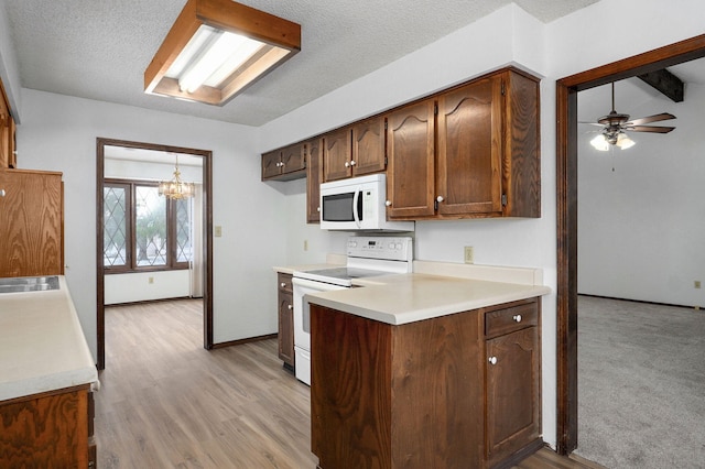 kitchen featuring white appliances, light countertops, a peninsula, and light wood finished floors